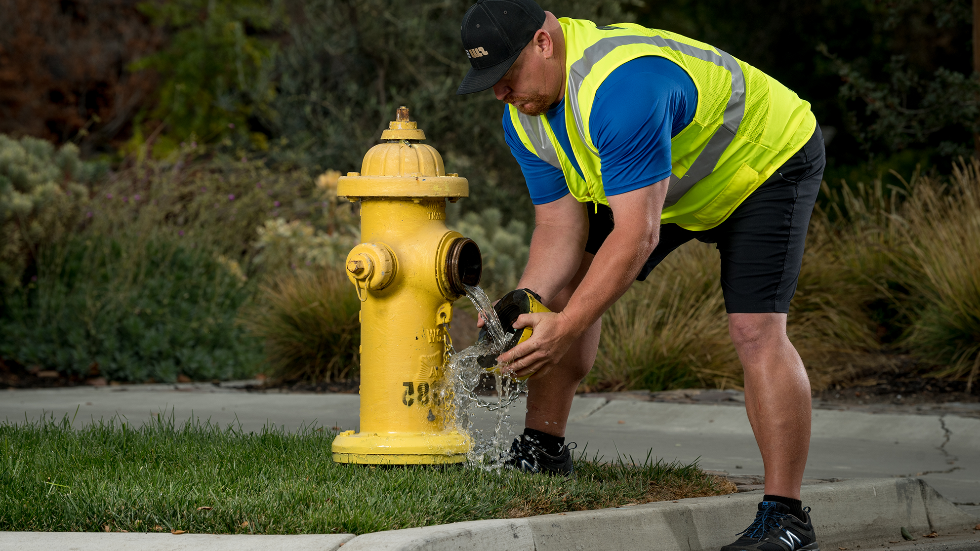 A San Jose Water employee removing the cap of a fire hydrant as some water leaks out.